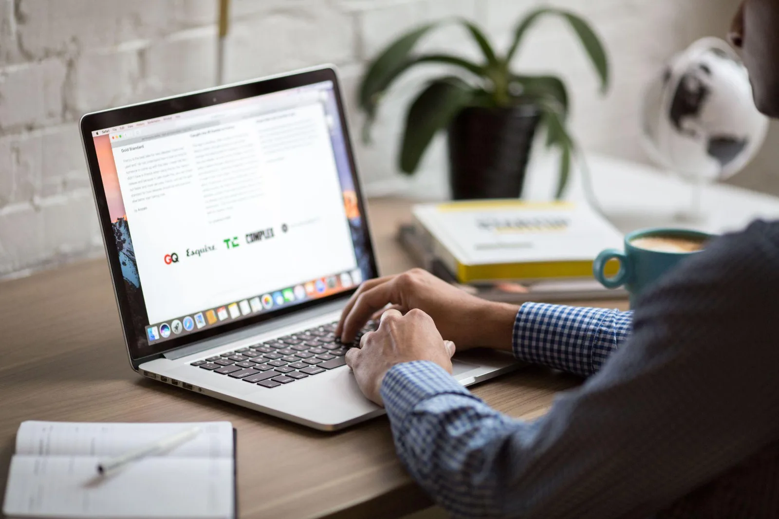 Writer drafting an article on a laptop at a desk with a notebook and coffee