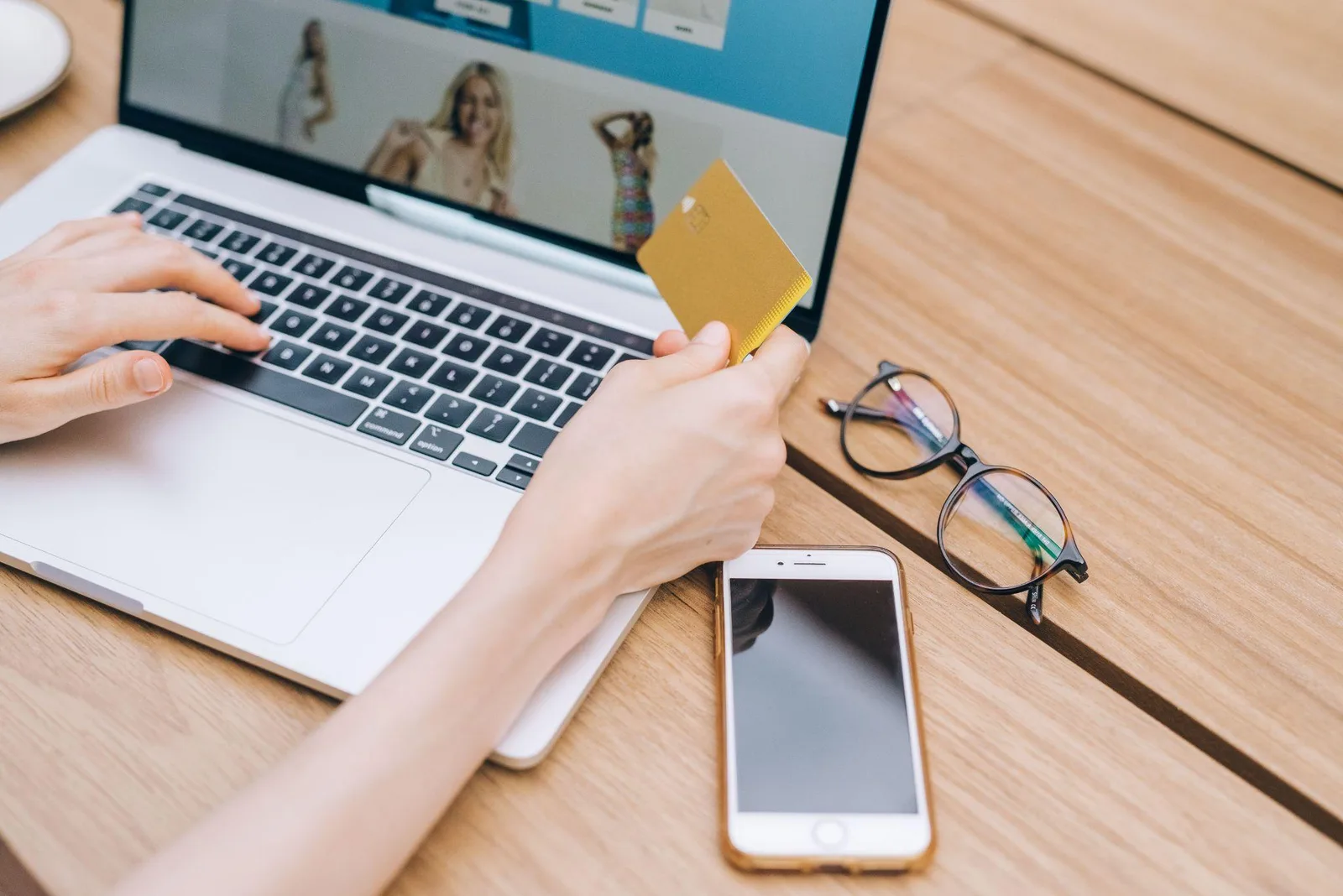 Shopper holding a credit card while browsing an online clothing store on a laptop