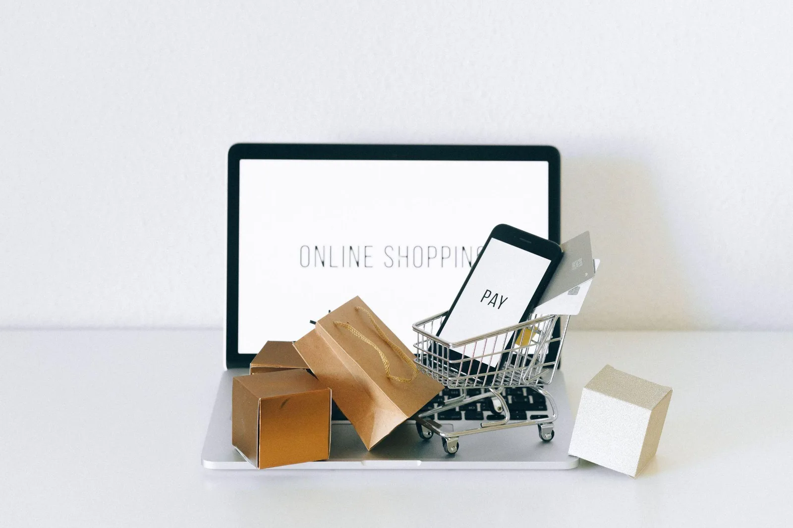 Miniature shopping trolley with parcels and a phone showing a pay screen on a laptop keyboard