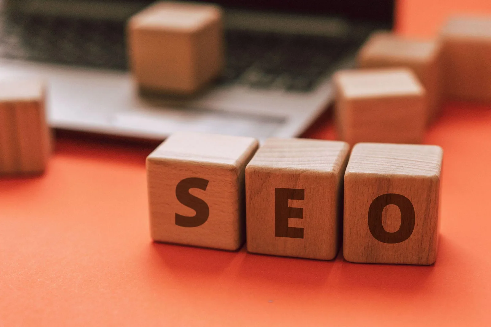 Wooden blocks spelling SEO in front of a laptop on an orange background
