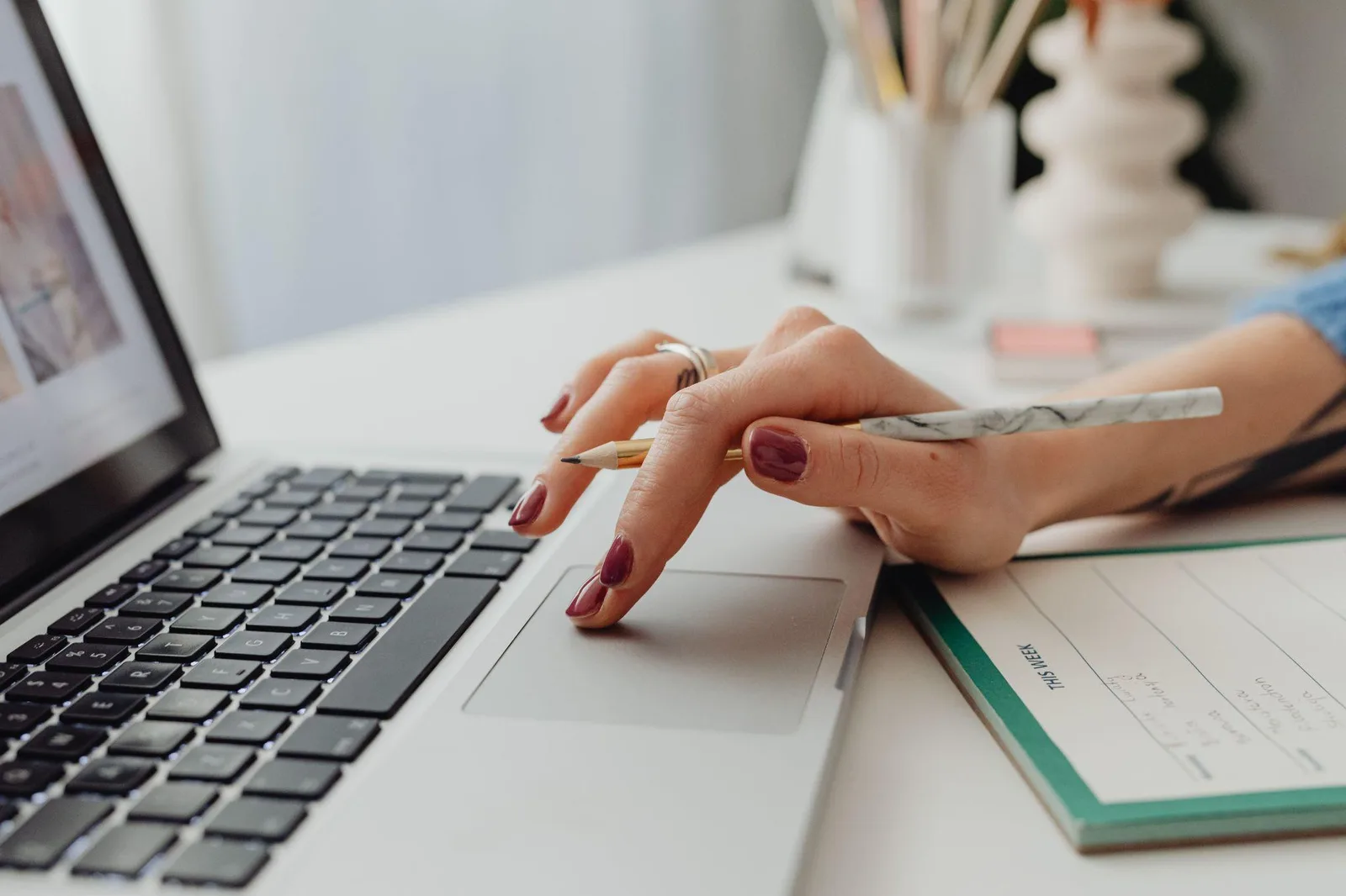 Writer resting a hand on a laptop trackpad beside a weekly planner and pencil